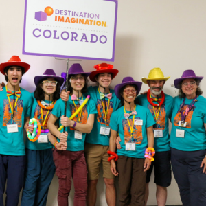 Kate Donelan (far right), Affiliate Director of Destination Imagination (DI) Colorado, poses with a DI Colorado team at Global Finals 2024.  They are all wearing matching aqua-colored DI Colorado t-shirts and wearing colorful cowboy hats. 