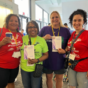 Tracy Ortiz (second from left), Team Manager for a Destination Imagination Michigan team, wearing a bright green shirt and posing with her DI Champion of Inclusion award certificate at Global Finals 2024. 